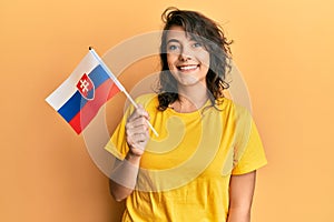 Young hispanic woman holding slovakia flag looking positive and happy standing and smiling with a confident smile showing teeth