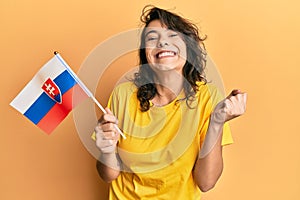 Mladá hispánka držiaca slovenskú vlajku hrdo kričiaca, oslavujúca víťazstvo a úspech veľmi vzrušená so zdvihnutou rukou