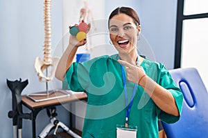 Young hispanic woman holding small balls to train hand muscle smiling happy pointing with hand and finger
