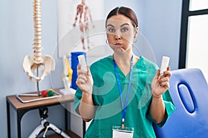 Young hispanic woman holding strip band for sprains puffing cheeks with funny face