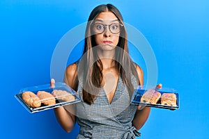 Young hispanic woman holding take away food puffing cheeks with funny face