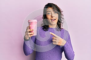 Young hispanic woman holding takeaway cup of coffee smiling happy pointing with hand and finger