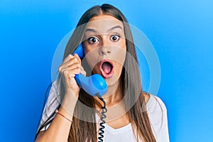 Young hispanic woman holding vintage telephone scared and amazed with open mouth for surprise, disbelief face