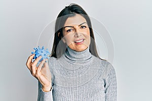 Young hispanic woman holding virus toy looking positive and happy standing and smiling with a confident smile showing teeth