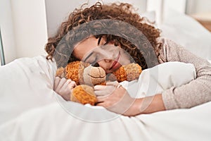 Young hispanic woman hugging teddy bear lying on bed sleeping at bedroom