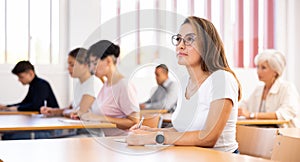 Young Hispanic woman listening to lecture and taking notes in classroom