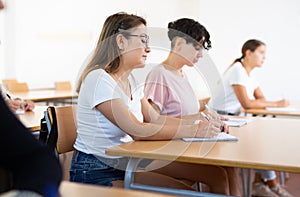 Young Hispanic woman listening to lecture and taking notes in classroom