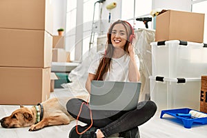 Young hispanic woman listening to music sitting on floor with dog at new home