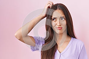 Young hispanic woman with long hair standing over pink background confuse and wondering about question