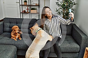 Young hispanic woman make selfie by the smartphone sitting on sofa with dogs at home