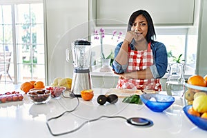 Young hispanic woman making healthy smoothie looking stressed and nervous with hands on mouth biting nails