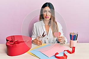 Young hispanic woman making valentine gift sitting on the table depressed and worry for distress, crying angry and afraid