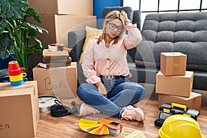Young hispanic woman moving to a new home sitting on the floor confuse and wondering about question