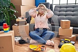 Young hispanic woman moving to a new home sitting on the floor crazy and scared with hands on head, afraid and surprised of shock