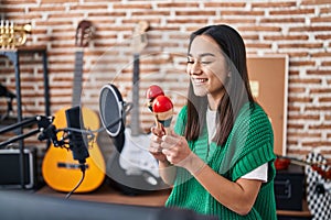 Young hispanic woman musician playing maracas at music studio