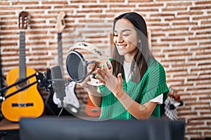 Young hispanic woman musician playing tambourine at music studio