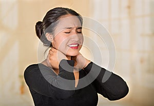 Young hispanic woman posing for camera showing signs of neck pain, holding hands on painful part of body, injury concept