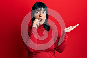 Young hispanic woman presenting with open palms, holding something afraid and shocked with surprise and amazed expression, fear