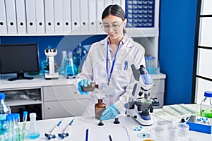 Young hispanic woman scientist measuring liquid at laboratory