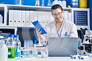Young hispanic woman scientist using laptop and touchpad at laboratory