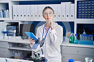 Young hispanic woman scientist using touchpad working at laboratory