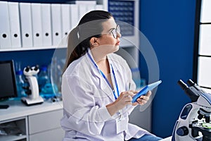 Young hispanic woman scientist using touchpad working at laboratory