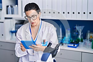 Young hispanic woman scientist using touchpad working at laboratory