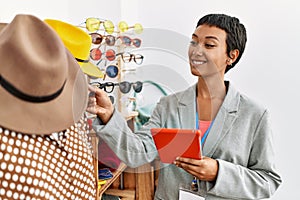 Young hispanic woman shopkeeper smiling confident using touchpad working at clothing store