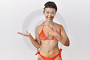 Young hispanic woman with short hair wearing bikini showing palm hand and doing ok gesture with thumbs up, smiling happy and
