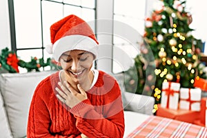 Young hispanic woman with short hair wearing christmas hat sitting on the sofa smiling and laughing hard out loud because funny