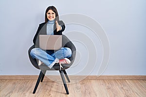 Young hispanic woman sitting on chair using computer laptop smiling friendly offering handshake as greeting and welcoming