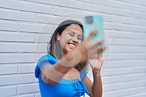 Young hispanic woman smiling confident having video call over white isolated brick background