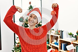 Young hispanic woman smiling confident holding christmas balls at home