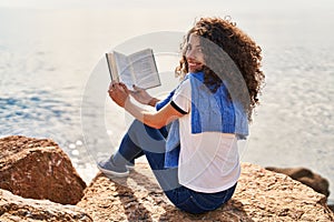 Young hispanic woman smiling confident reading book at seaside