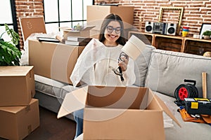 Young hispanic woman smiling confident unpacking cardboard box at new home