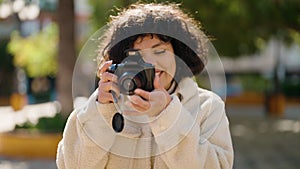 Young hispanic woman smiling confident using professional camera at park