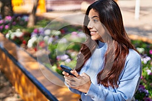 Young hispanic woman smiling confident using smartphone at park