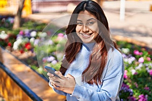 Young hispanic woman smiling confident using smartphone at park