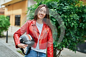 Young hispanic woman smiling happy holding moto helmet at the city