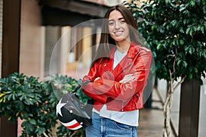 Young hispanic woman smiling happy holding moto helmet at the city