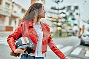 Young hispanic woman smiling happy holding moto helmet at the city