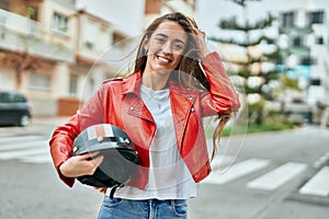 Young hispanic woman smiling happy holding moto helmet at the city