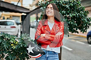 Young hispanic woman smiling happy holding moto helmet at the city