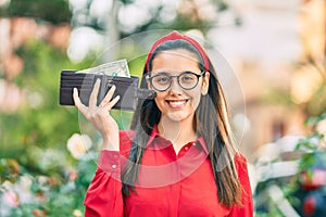 Young hispanic woman smiling happy holding wallet with one dollar at the city