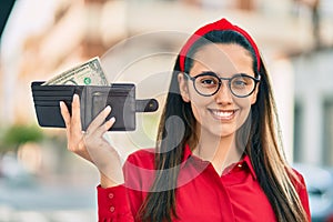 Young hispanic woman smiling happy holding wallet with one dollar at the city