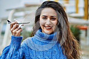 Young hispanic woman smiling happy plane toy at the city