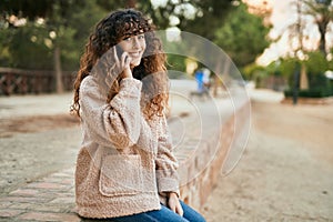 Young hispanic woman smiling happy talking on the smartphone at the park