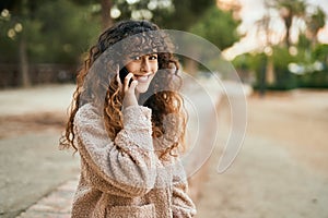 Young hispanic woman smiling happy talking on the smartphone at the park