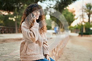 Young hispanic woman smiling happy talking on the smartphone at the park