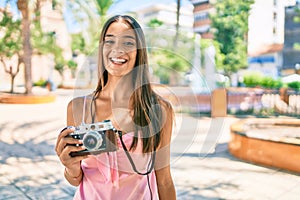 Young hispanic woman smiling happy using vintage camera standing at the park